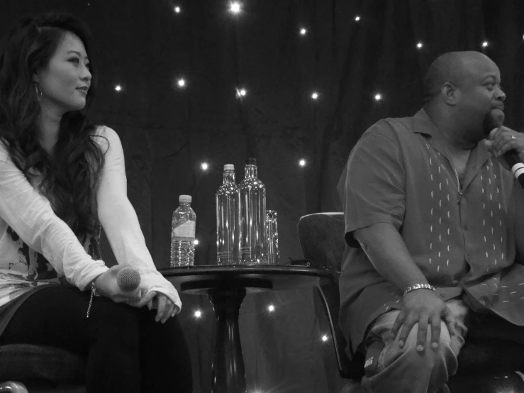 a woman sits on a stool talking to a man with a microphone