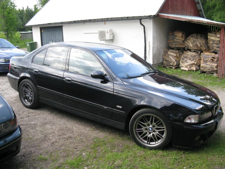 a black bmw parked next to several trees in a yard