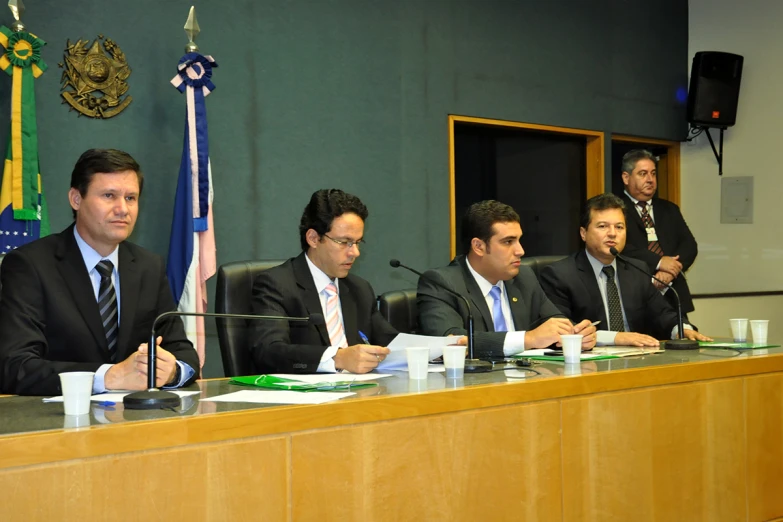 a number of men sitting at a desk with papers