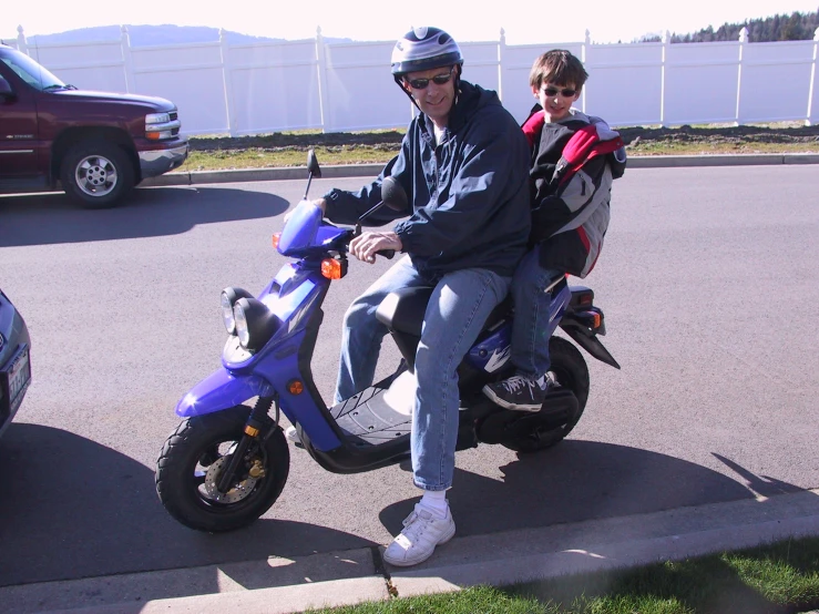 two people sitting on a blue scooter with two wheels