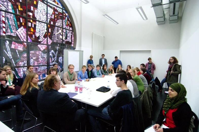 some people sitting at long tables in front of a large stained glass window