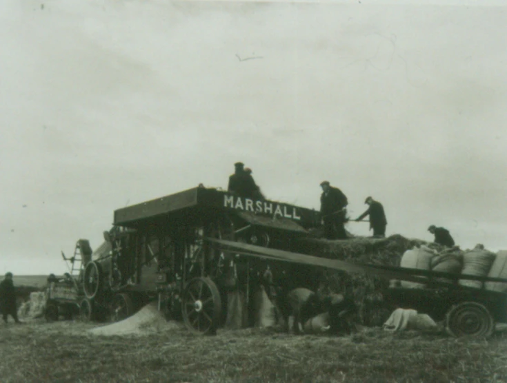 men standing near an old farm tractor loaded with hay