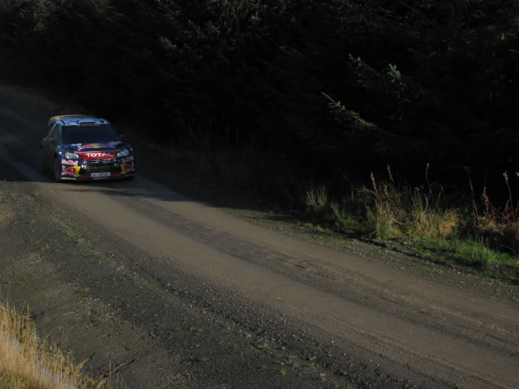 a rally car driving down a dirt road near trees