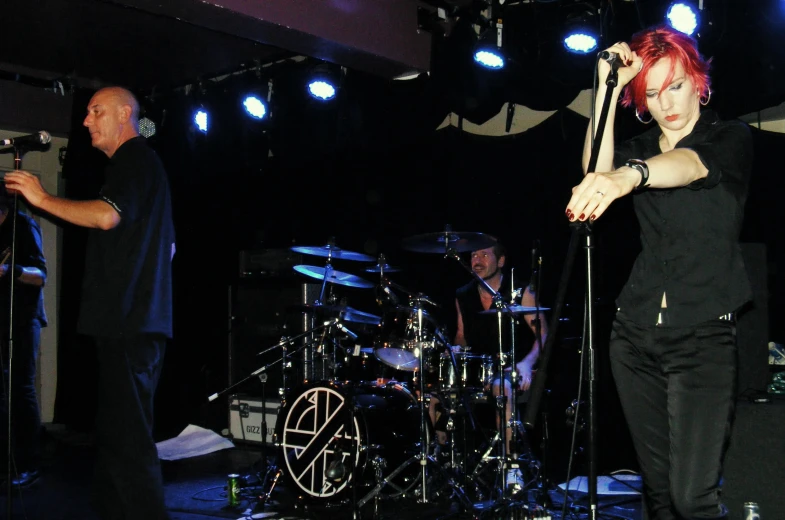 a man holding a microphone and a woman standing by a drum kit