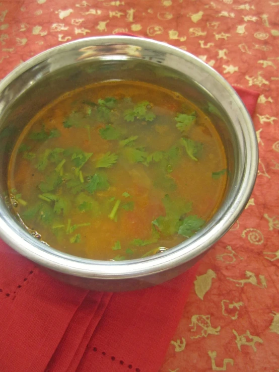 soup sits in a silver bowl on a red cloth