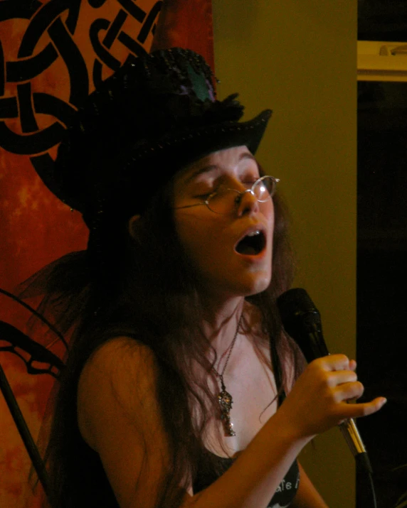 a woman in glasses and a hat speaks into a microphone