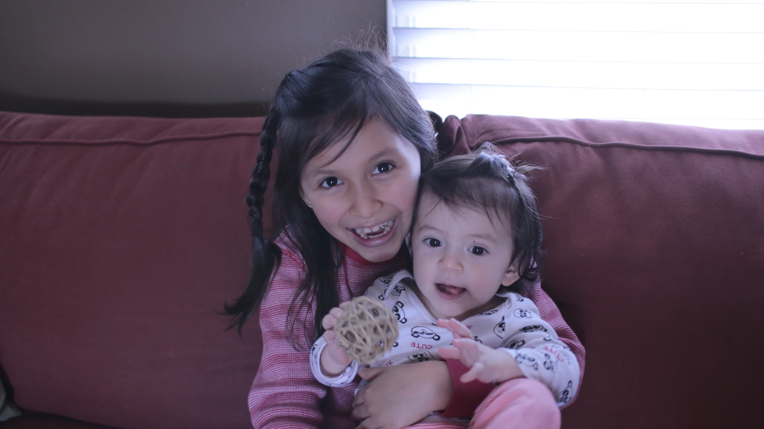 two girls smiling and holding onto one another while sitting on the couch