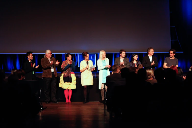 several people standing at a podium on stage, all with microphones