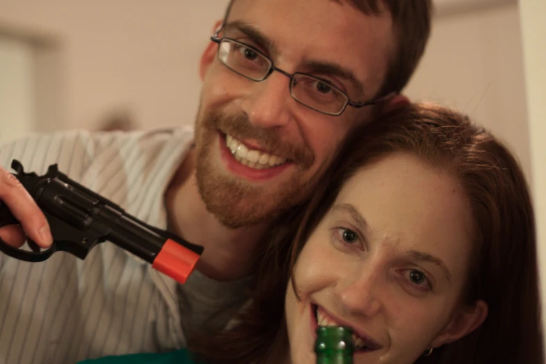 a man and woman smiling while holding a gun in front of them