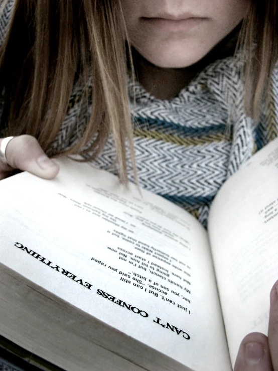 a girl holding a book and reading it while looking at the camera