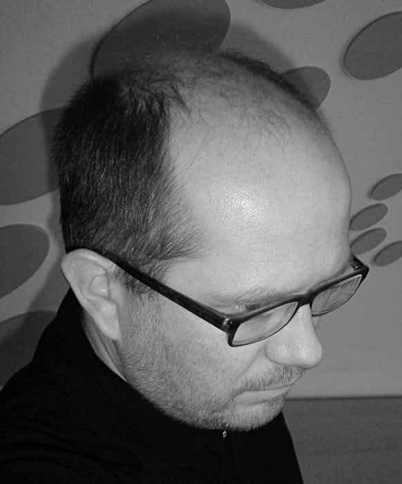 a bald man wearing glasses next to a wall with circles