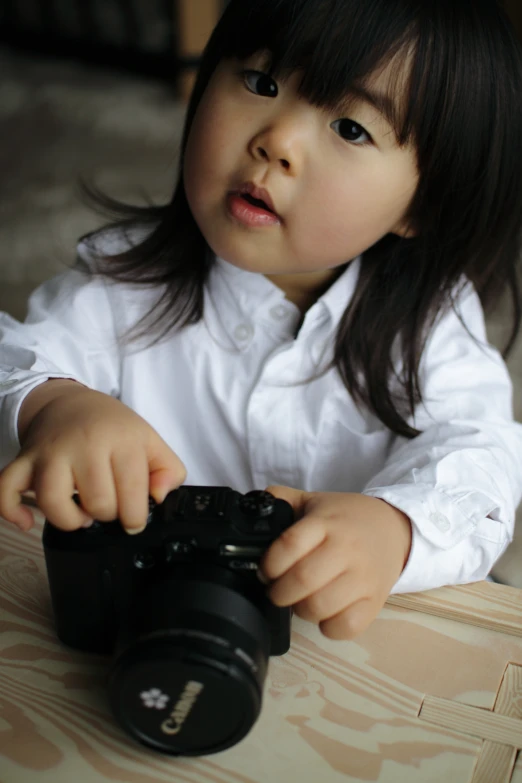 a little girl holding a camera on the table