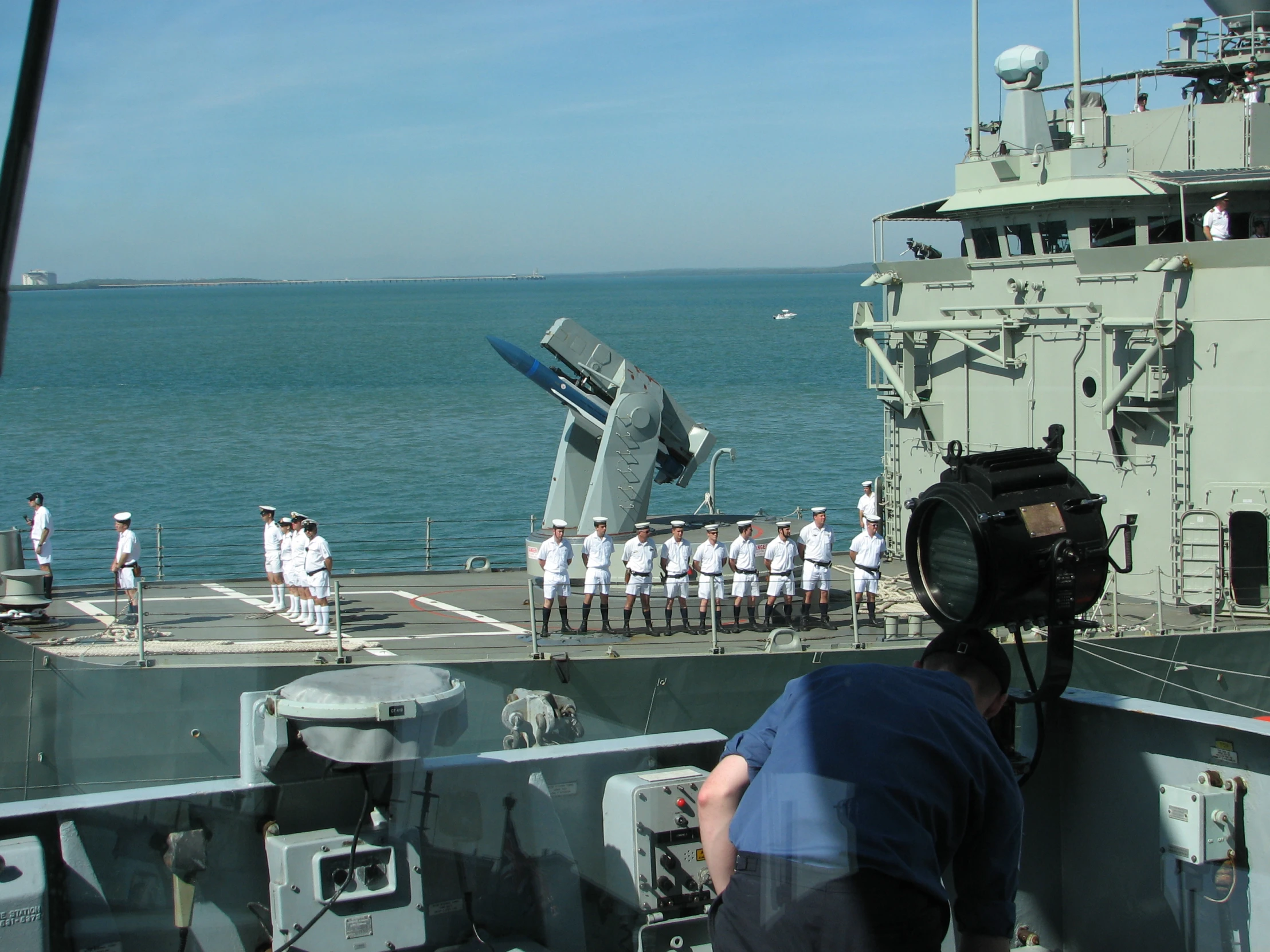 a cameraman in blue shirt and white suit standing on the deck of a ship