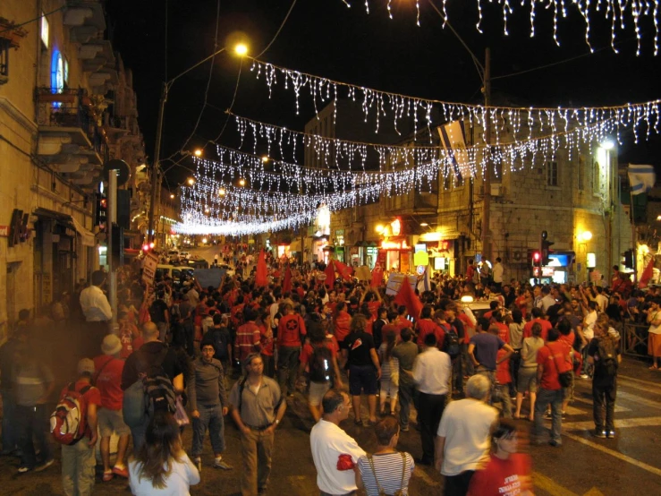 a crowded street at night with people walking and onlookers