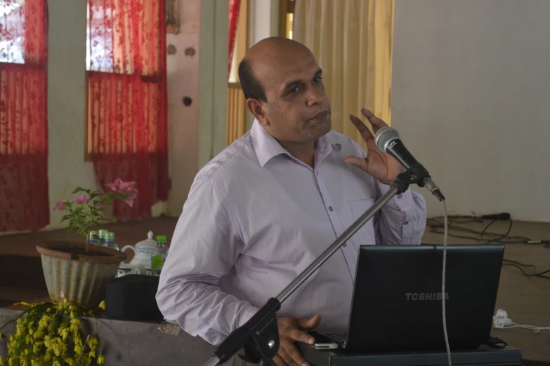 man speaking into microphone and holding computer in hands