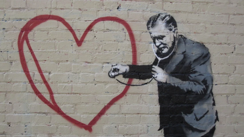 a man holding a knife and pointing at a heart spray painted on the wall