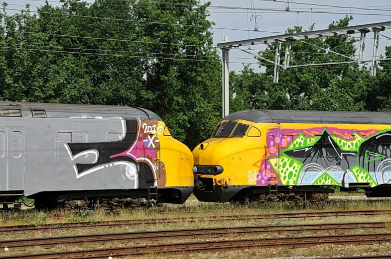 two trains covered in colorful graffiti sitting on train tracks