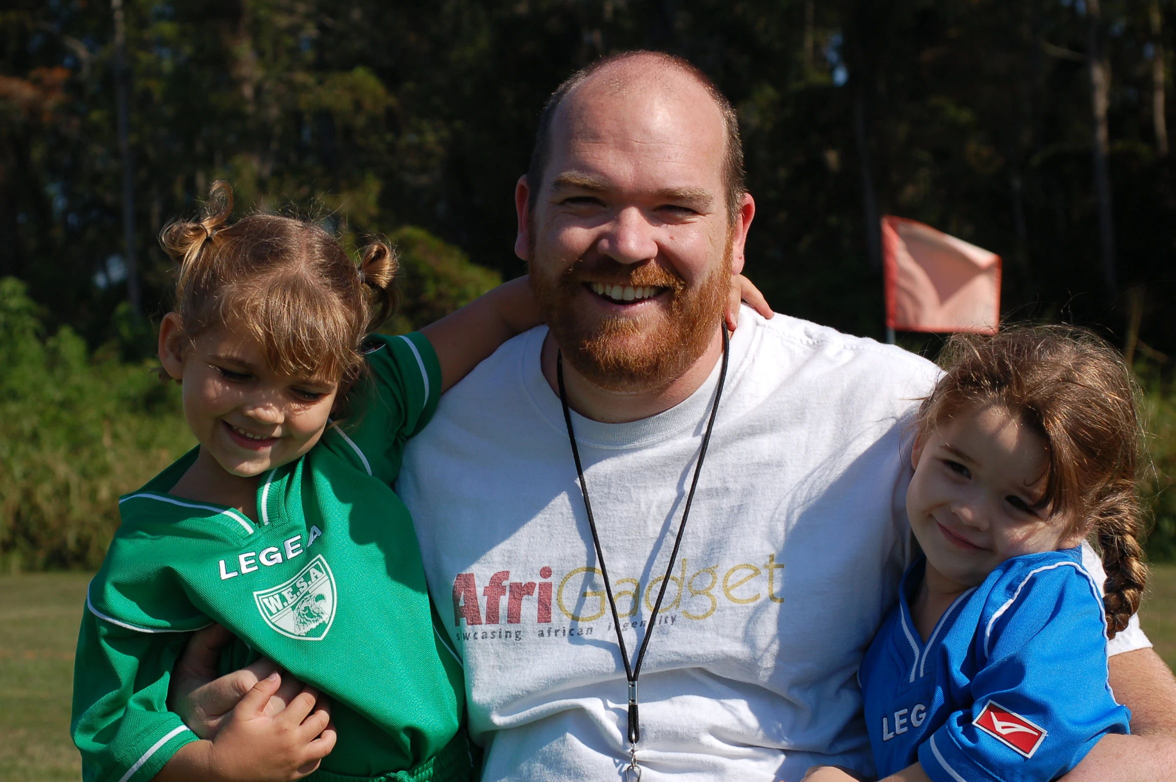 a man sits next to two little girls and the man is holding a frisbee