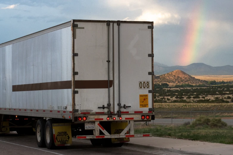 a semi truck with a rainbow behind it