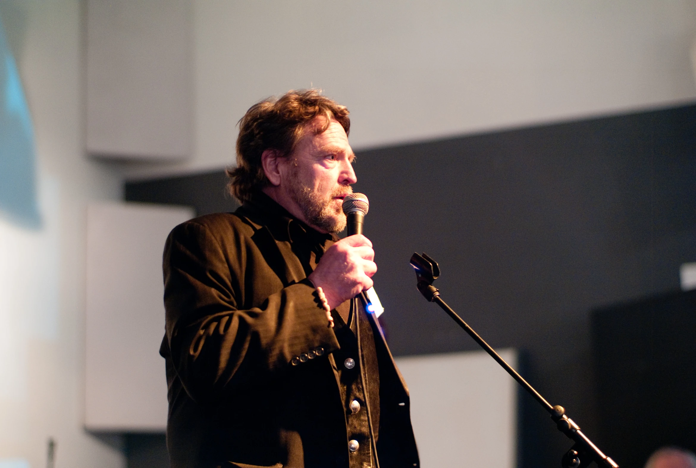 a man holding a microphone stands in front of a stage and talks into the microphone