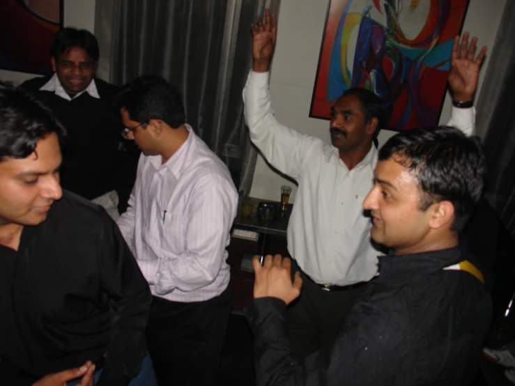 several men sit in the middle of a room and one man holds his hand up