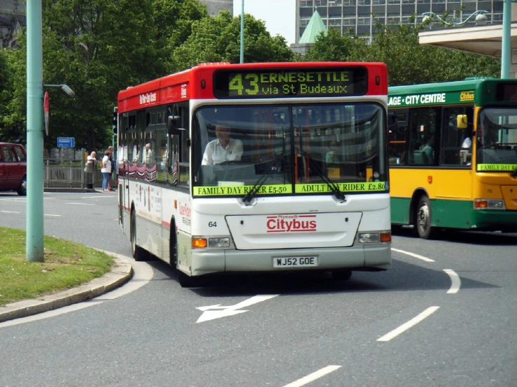 buses drive past an intersection with green trees and buildings
