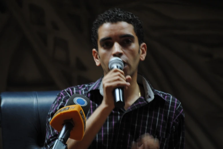 a man in a plaid shirt sitting down with a microphone