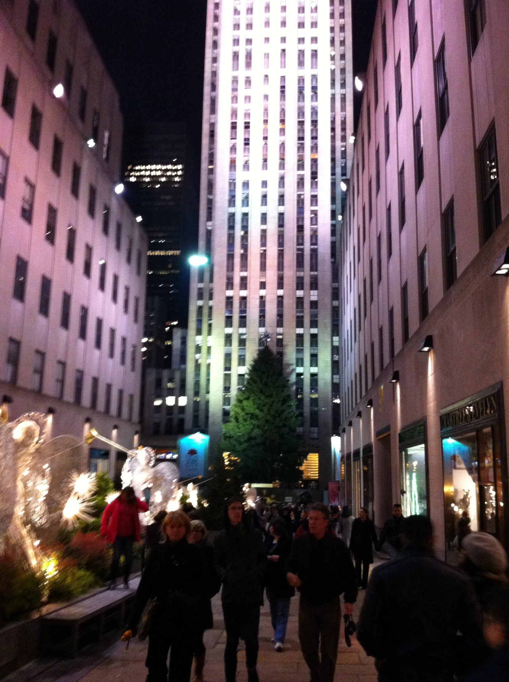 a group of people walking down the sidewalk in a city at night