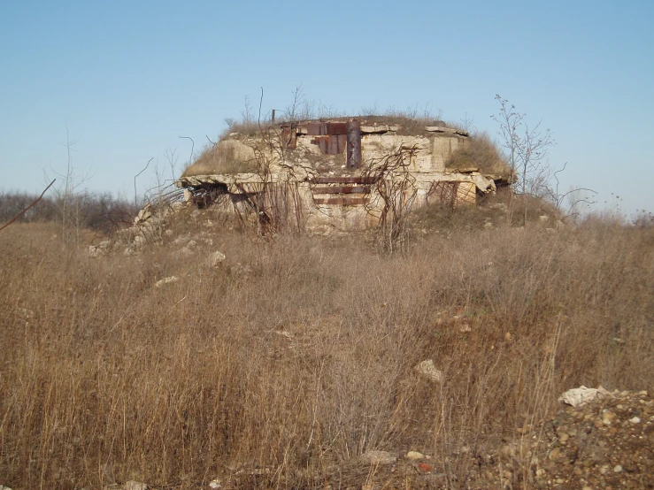 a derelict house sits in the middle of a brown field