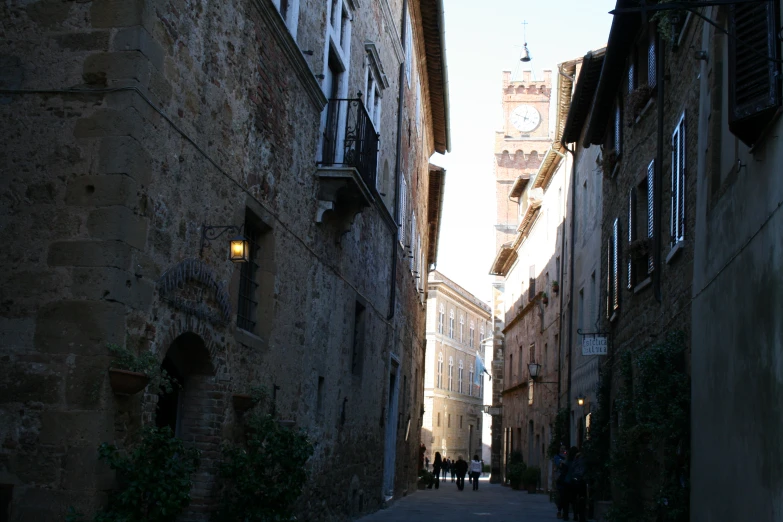 looking down an alleyway from the side with people walking up one side and a clock tower behind