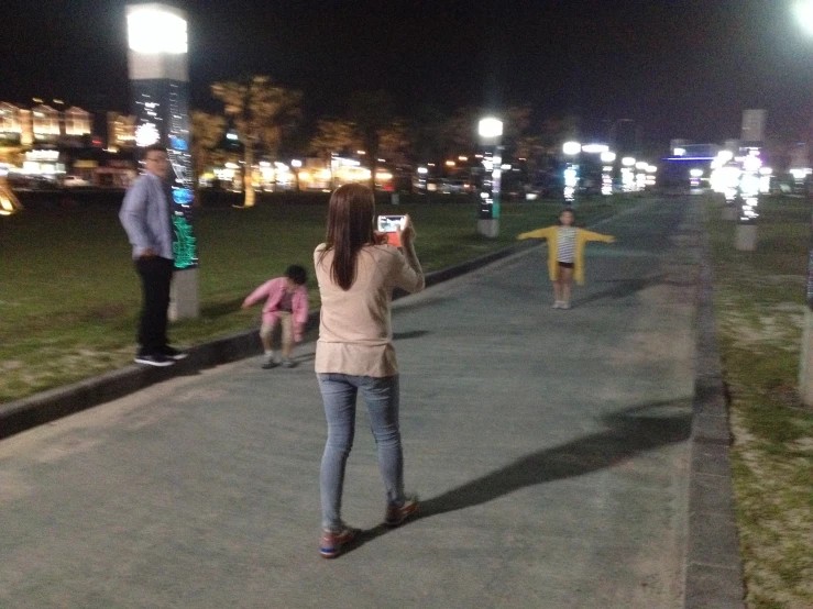 a woman holding up her cell phone with some lights in the background