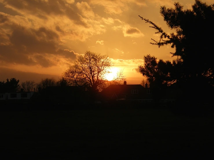 the sun is setting behind the clouds above trees