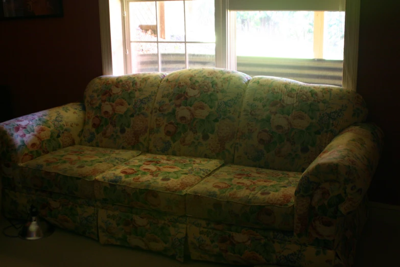 a floral couch is by the window with blind