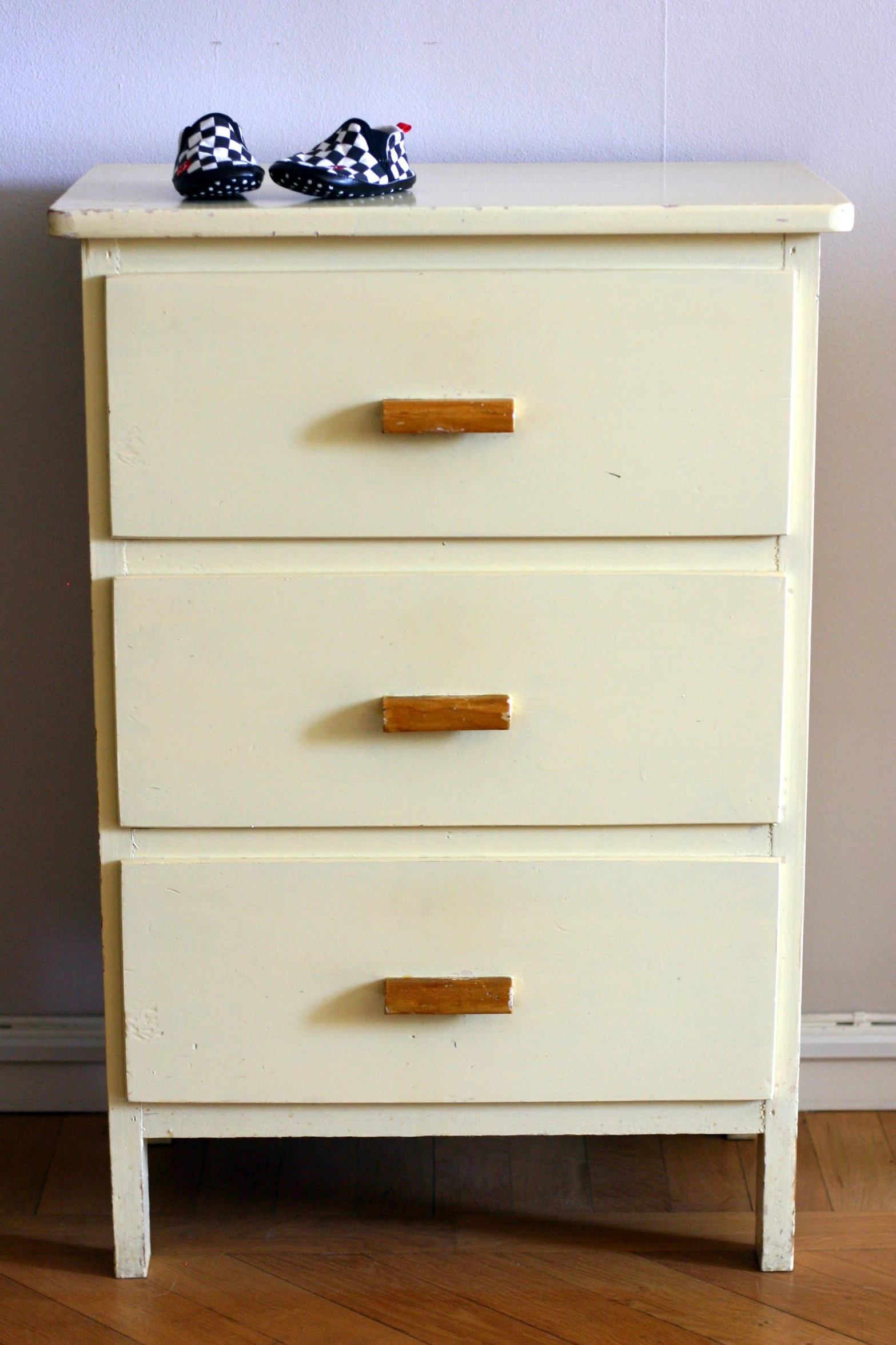 a white chest with wooden legs and three drawers