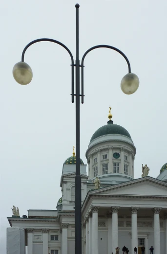 there are two street lights on one pole in front of the white building