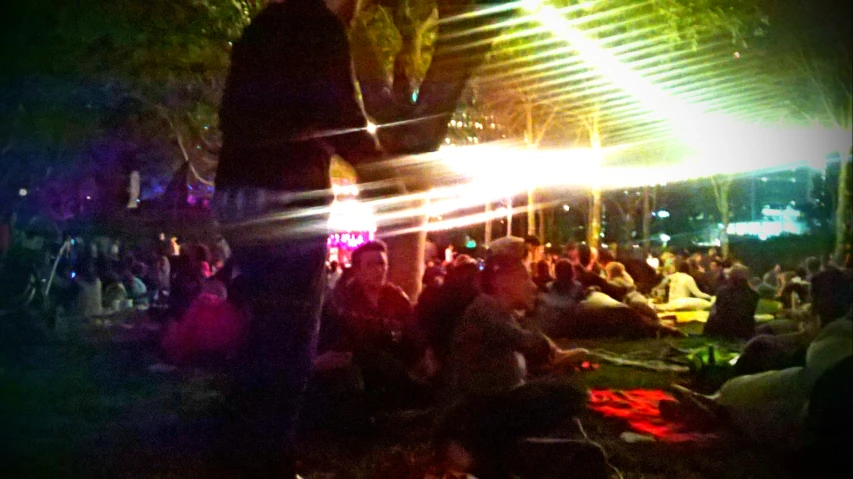 crowd sitting outside at night, having a party