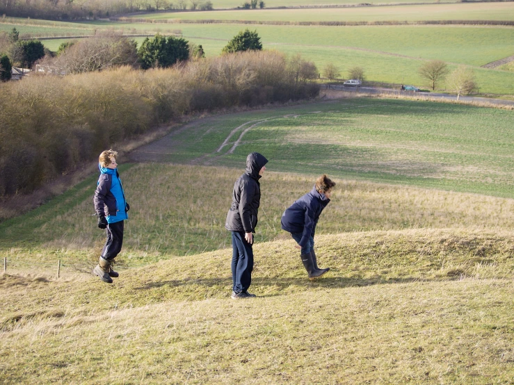 three people standing on top of a grass covered hillside