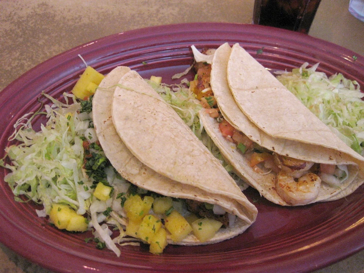 two tacos sitting on top of a plate with fruit