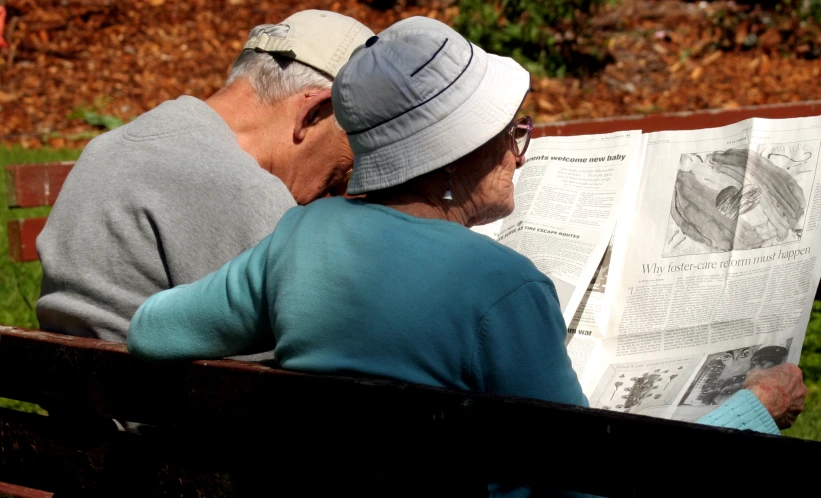 two elderly men are sitting on a bench reading a newspaper