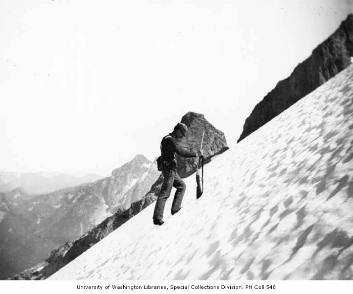 a man with backpack walking up the side of a snow covered mountain