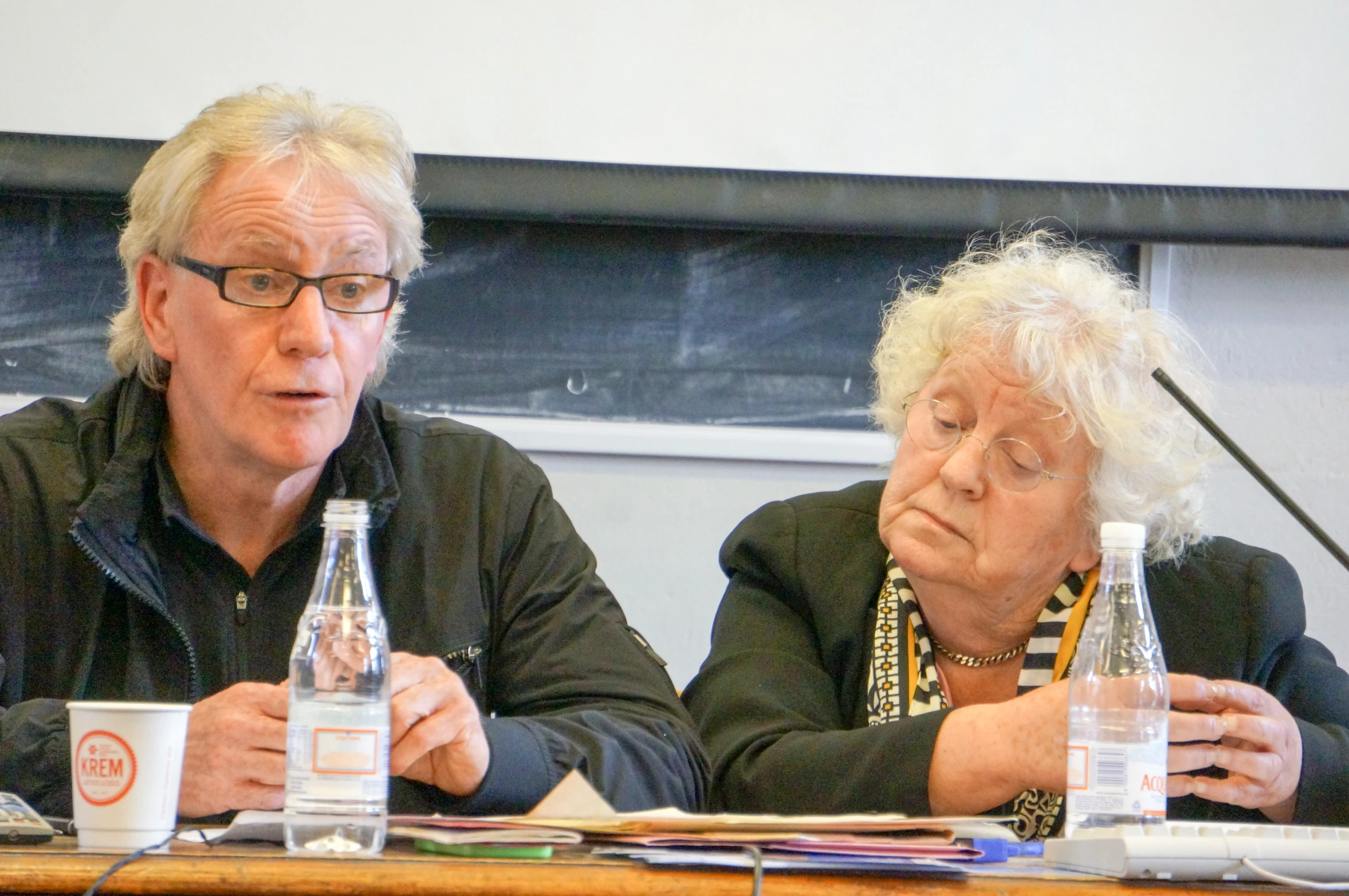 man and woman are sitting at a table with water bottles