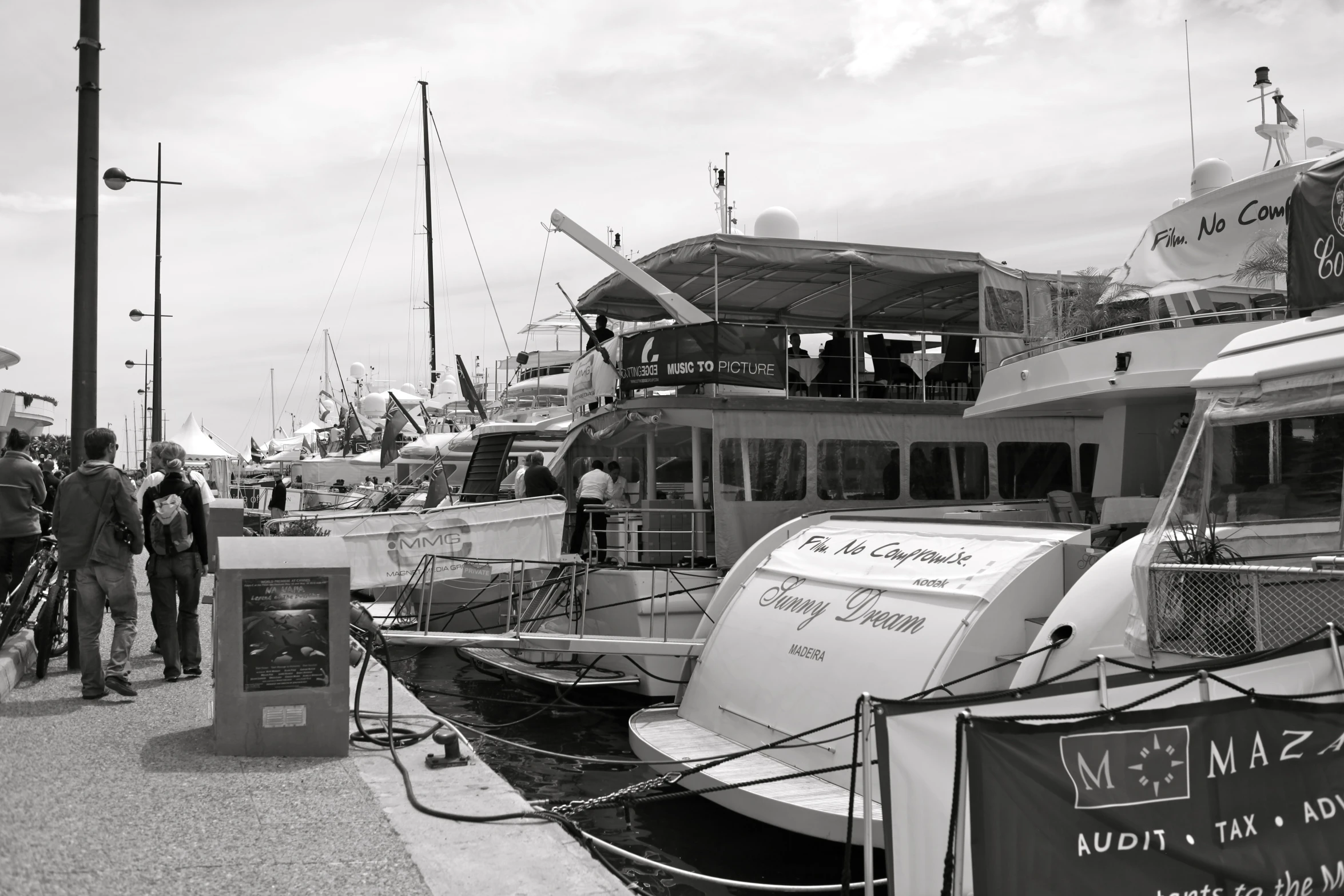 many boats are docked near the dock while people walk by