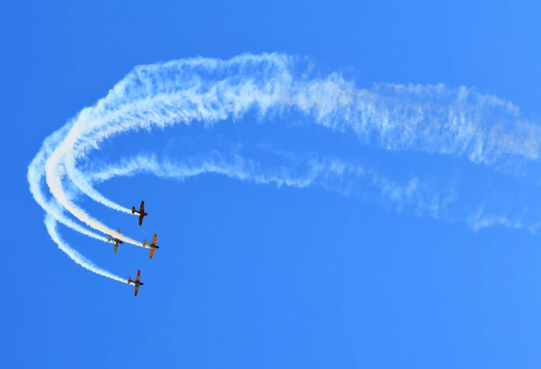 four airplanes fly through a blue sky leaving white smoke behind them