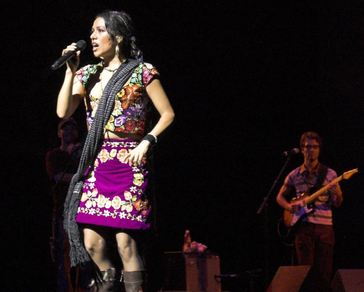 a woman standing on stage wearing a dress and boots