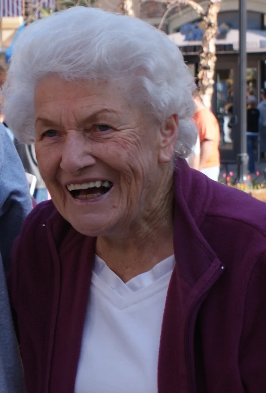 an older woman laughs while standing in front of people