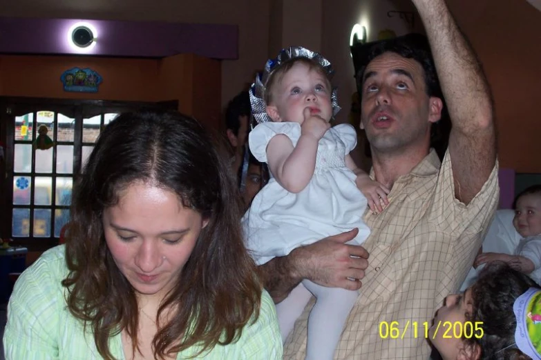 two adults are watching as a baby reaches up to touch the hair of an adult