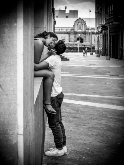 black and white po of two people kissing while standing on a wall
