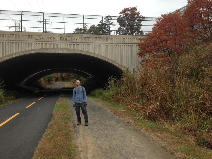 a man standing in the middle of a road looking up at a bridge