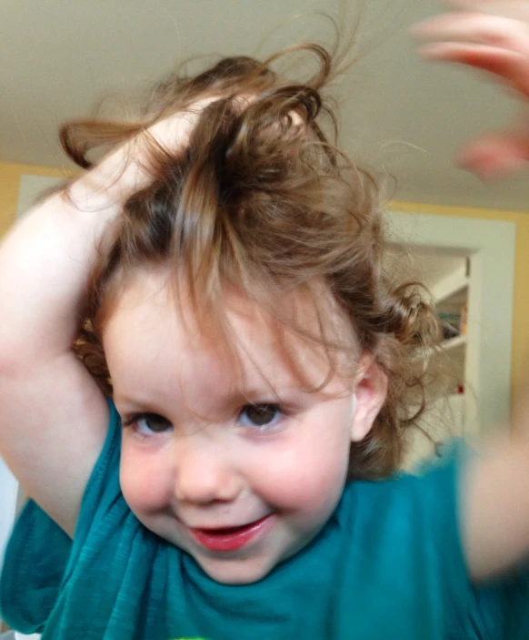 a little girl wearing a blue shirt holding her hair up