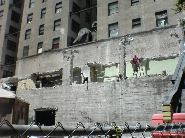 the side of a building with an unfinished brick wall and people standing at the window